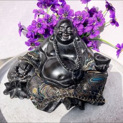 Glad, siddende lykkebuddha i sort polyresin med farverige m�nsterdetaljer, perlek�de og en kinesisk guldbarre i h�nden.