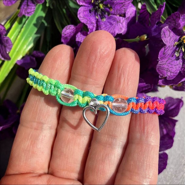 Armbnd, hndlavet af Krystal Oasen med bjergkrystal (6,5 mm) og slvfarvet hjerte charm. Justerbar regnbuefarvet og hvid nylonsnor, ca. 7 mm bredt.
