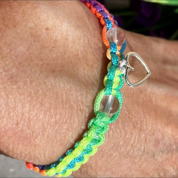 Armbnd, hndlavet af Krystal Oasen med bjergkrystal (6,5 mm) og slvfarvet hjerte charm. Justerbar regnbuefarvet og hvid nylonsnor, ca. 7 mm bredt.