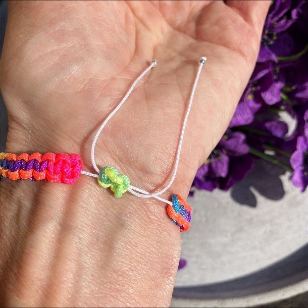 Armbnd, hndlavet af Krystal Oasen med bjergkrystal (6,5 mm) og slvfarvet hjerte charm. Justerbar regnbuefarvet og hvid nylonsnor, ca. 7 mm bredt.