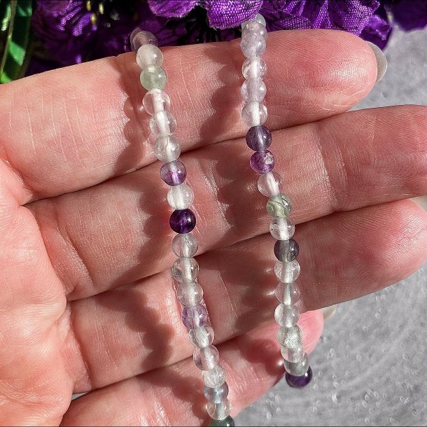 To spinkle regnbue fluorit armb�nd med 4 mm transparente perler i lilla og gr�nne nuancer holdt over fingrene for at vise det fine farvespil.