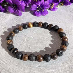 Armb�nd med brune tiger�je krystalperler og sorte lavasten liggende fladt p� en gr� baggrund med lilla blomster.
