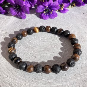 Armb�nd med brune tiger�je krystalperler og sorte lavasten liggende fladt p� en gr� baggrund med lilla blomster.