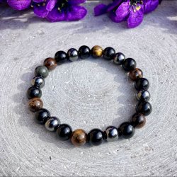 Krystalarmb�nd med tiger�je, obsidian og h�matit perler p� r�, gr� stenbaggrund.