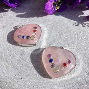 Hjerteformede rosakvarts vedh�ng med de syv chakra sten fotograferet p� en gr� baggrund med lilla blomster.